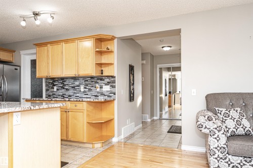 Kitchen with open shelves, light wood finish cabinets, stainless steel fridge, a textured ceiling, and light stone counters - 192 Keyport Circle, Leduc, AB - Indoor