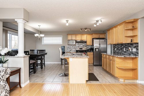 Kitchen featuring open shelves, light stone countertops, stainless steel appliances, a breakfast bar area, and a textured ceiling - 192 Keyport Circle, Leduc, AB - Indoor Photo Showing Kitchen