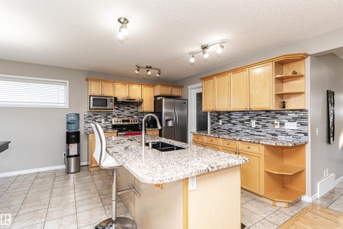 Kitchen with open shelves, light wood finish cabinetry, stainless steel appliances, light stone countertops, and a breakfast bar area - 192 Keyport Circle, Leduc, AB - Indoor Photo Showing Kitchen With Double Sink