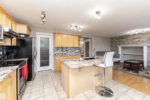 Kitchen with track lighting, stainless steel electric range oven, light wood finish cabinetry, light tile patterned flooring, and a kitchen breakfast bar - 192 Keyport Circle, Leduc, AB - Indoor Photo Showing Kitchen