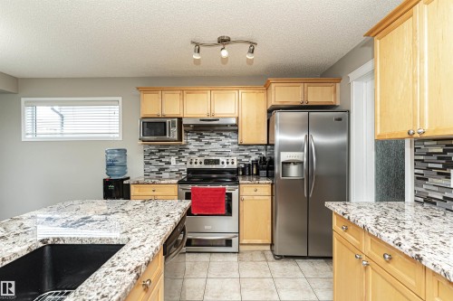 Kitchen featuring stainless steel appliances, light wood finish cabinetry, light stone counters, light tile patterned flooring, and tasteful backsplash - 192 Keyport Circle, Leduc, AB - Indoor Photo Showing Kitchen With Stainless Steel Kitchen With Upgraded Kitchen