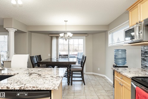Kitchen featuring light stone countertops, suspended lighting, stainless steel appliances, a textured ceiling, and light wood finish cabinetry - 192 Keyport Circle, Leduc, AB - Indoor