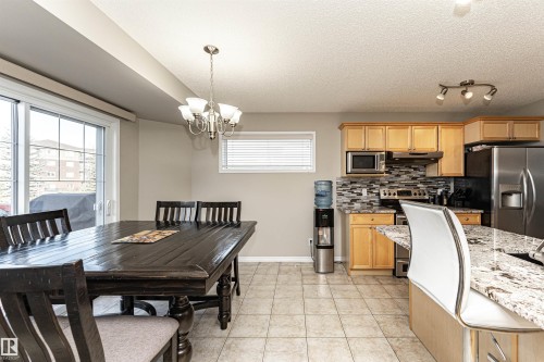 Kitchen with backsplash, light stone countertops, stainless steel appliances, suspended lighting, and light wood finish cabinetry - 192 Keyport Circle, Leduc, AB - Indoor Photo Showing Dining Room