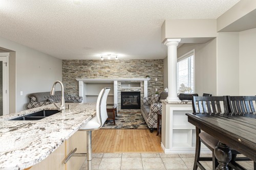 Kitchen with a tile fireplace, light stone countertops, light wood finish cabinets, a textured ceiling, and open floor plan - 192 Keyport Circle, Leduc, AB - Indoor Photo Showing Kitchen With Fireplace With Double Sink