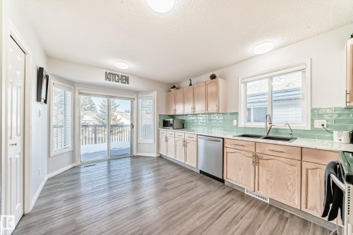 Kitchen with light wood finish cabinets, stainless steel appliances, decorative backsplash, light wood-style floors, and a textured ceiling - 6 Jefferson Road, Edmonton, AB 