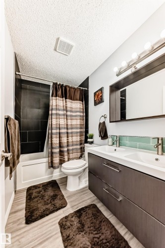 Bathroom featuring double vanity, shower / bath combination with curtain, a textured ceiling, and light wood-style floors - 6 Jefferson Road, Edmonton, AB 
