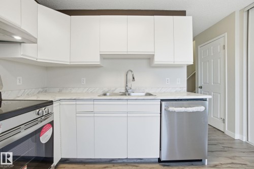 Kitchen with stainless steel appliances, light countertops, white cabinets, a textured ceiling, and light wood-style flooring - 8006 15A Avenue, Edmonton, AB - Indoor Photo Showing Kitchen With Double Sink
