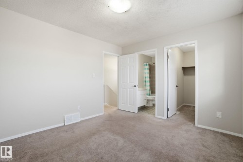 Unfurnished bedroom with a walk in closet, light colored carpet, a textured ceiling, and ensuite bathroom - 8006 15A Avenue, Edmonton, AB - Indoor Photo Showing Other Room