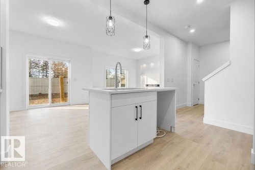 Kitchen featuring light wood-type flooring, decorative light fixtures, white cabinetry, and a kitchen island - 235 Linden Loop, Leduc, AB - Indoor Photo Showing Other Room