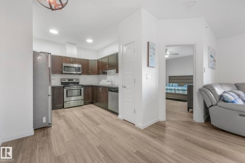 Kitchen featuring open floor plan, appliances with stainless steel finishes, dark brown cabinets, decorative backsplash, and light wood-type flooring - 419 396 Silverberry Road, Edmonton, AB - Indoor Photo Showing Kitchen