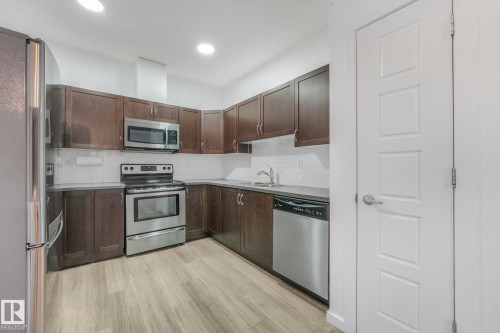 Kitchen with dark brown cabinetry, stainless steel appliances, decorative backsplash, light countertops, and light wood-type flooring - 419 396 Silverberry Road, Edmonton, AB - Indoor Photo Showing Kitchen With Double Sink