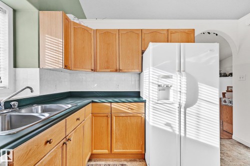 Kitchen featuring white fridge with ice dispenser, dark countertops, and tasteful backsplash - 2 Creekside Way, Spruce Grove, AB - Indoor Photo Showing Kitchen With Double Sink