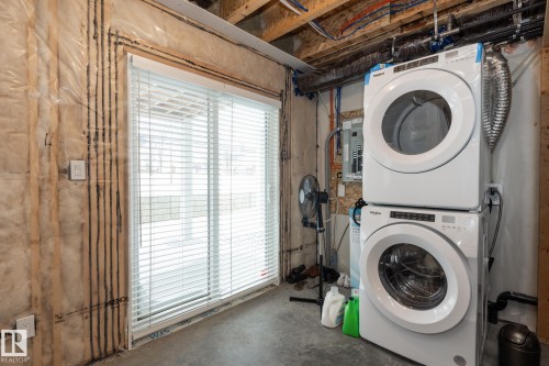 Laundry area featuring unfinished concrete floors, stacked washer / dryer, and electric panel - 56 320 Secord Boulevard, Edmonton, AB - Indoor Photo Showing Laundry Room