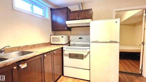 Kitchen with white appliances, dark wood finish cabinets, and light wood-style floors - 4709 106 Street, Edmonton, AB - Indoor Photo Showing Kitchen