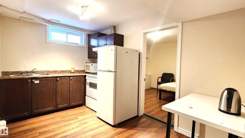Kitchen featuring white appliances, light wood finished floors, and dark wood finish cabinetry - 4709 106 Street, Edmonton, AB - Indoor Photo Showing Kitchen With Double Sink