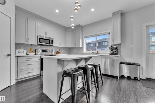 Kitchen featuring stainless steel appliances, a kitchen bar, white cabinetry, dark wood finished floors, and a center island - 906 Berg Place, Leduc, AB - Indoor Photo Showing Kitchen With Upgraded Kitchen