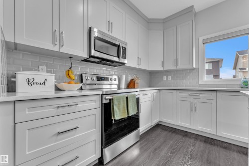 Kitchen with stainless steel appliances, white cabinetry, light stone counters, dark wood-type flooring, and tasteful backsplash - 906 Berg Place, Leduc, AB - Indoor Photo Showing Kitchen