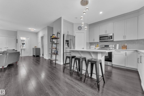 Kitchen with a kitchen bar, stainless steel appliances, white cabinets, a center island, and dark wood-type flooring - 906 Berg Place, Leduc, AB - Indoor Photo Showing Kitchen With Upgraded Kitchen