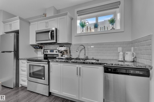 Kitchen with stainless steel appliances, white cabinets, dark stone countertops, and dark wood-style flooring - 906 Berg Place, Leduc, AB - Indoor Photo Showing Kitchen With Upgraded Kitchen
