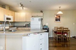 Kitchen with white appliances, a peninsula, dark wood-style flooring, a textured ceiling, and light wood finish cabinetry - 