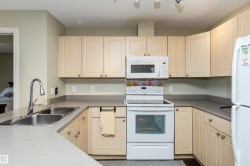 Kitchen featuring white appliances, a textured ceiling, and light wood finish cabinetry - 
