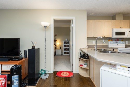 Kitchen with light countertops, white appliances, light wood finish cabinetry, dark wood-style floors, and a textured ceiling - 314 4403 23 Street, Edmonton, AB - Indoor Photo Showing Kitchen With Double Sink