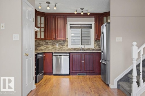 Kitchen with dark stone countertops, stainless steel appliances, reddish brown cabinets, backsplash, and light wood-style flooring - 736 Johns Road, Edmonton, AB - Indoor Photo Showing Kitchen