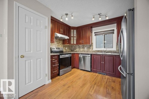 Kitchen with dark stone countertops, stainless steel appliances, light wood finished floors, glass fronted cabinets, and decorative backsplash - 736 Johns Road, Edmonton, AB - Indoor Photo Showing Kitchen