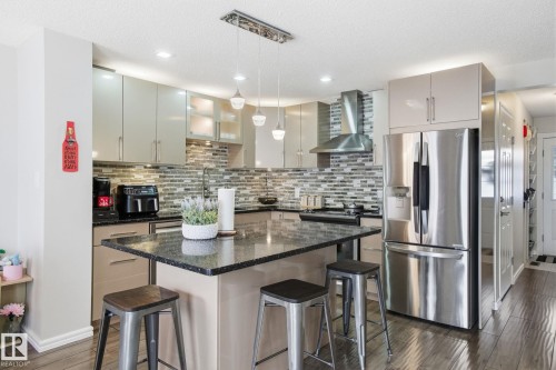 Kitchen with a kitchen bar, stainless steel appliances, pendant lighting, dark wood-style floors, and dark stone counters - 64 2004 Grantham Court, Edmonton, AB - Indoor