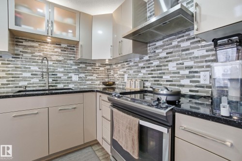 Kitchen with stainless steel electric range, dark stone counters, glass insert cabinets, and decorative backsplash - 64 2004 Grantham Court, Edmonton, AB - Indoor Photo Showing Kitchen With Upgraded Kitchen