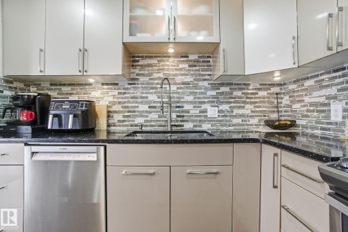 Kitchen with stainless steel dishwasher, glass fronted cabinets, dark stone countertops, and white cabinetry - 64 2004 Grantham Court, Edmonton, AB - Indoor Photo Showing Kitchen With Upgraded Kitchen
