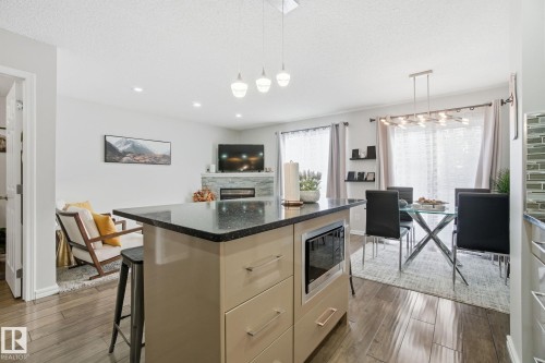 Kitchen with light wood finish cabinets, dark stone counters, dark wood finished floors, a kitchen island, and decorative light fixtures - 64 2004 Grantham Court, Edmonton, AB - Indoor
