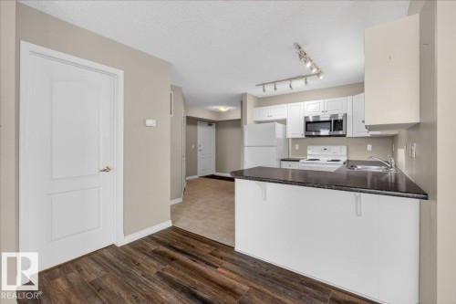 Kitchen featuring dark countertops, white appliances, white cabinets, a breakfast bar area, and a textured ceiling - 402 10649 Saskatchewan Drive, Edmonton, AB - Indoor Photo Showing Kitchen