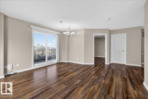Unfurnished living room with a chandelier, a textured ceiling, dark wood-style floors, and a city view - 402 10649 Saskatchewan Drive, Edmonton, AB - Indoor