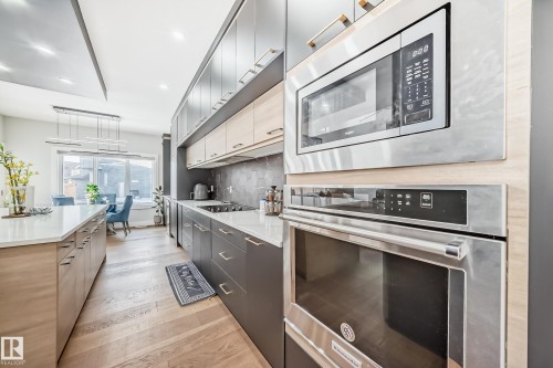 Two tone kitchen featuring stainless steel appliances, two tone color scheme, modern cabinets, decorative light fixtures, and light wood finished floors - 17112 68 Street, Edmonton, AB - Indoor Photo Showing Kitchen With Upgraded Kitchen