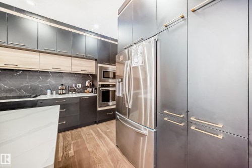 Kitchen featuring stainless steel appliances, light wood-type flooring, modern cabinets, backsplash, and light stone counters - 17112 68 Street, Edmonton, AB - Indoor Photo Showing Kitchen