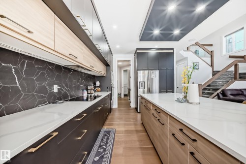 Two tone kitchen featuring two tone cabinets, modern cabinets, light stone counters, recessed lighting, and stainless steel fridge with ice dispenser - 17112 68 Street, Edmonton, AB - Indoor Photo Showing Kitchen With Upgraded Kitchen