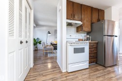 Kitchen featuring white electric range oven, under cabinet range hood, freestanding refrigerator, light wood-style floors, and backsplash - 