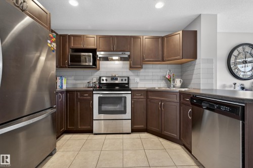 Kitchen featuring stainless steel appliances, dark brown cabinets, under cabinet range hood, dark countertops, and a textured ceiling - 5256 21 Avenue, Edmonton, AB - Indoor Photo Showing Kitchen