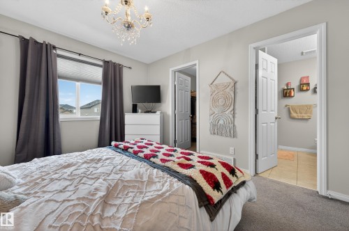 Bedroom with a spacious closet, light colored carpet, a chandelier, light tile patterned floors, and a textured ceiling - 5256 21 Avenue, Edmonton, AB - Indoor Photo Showing Bedroom