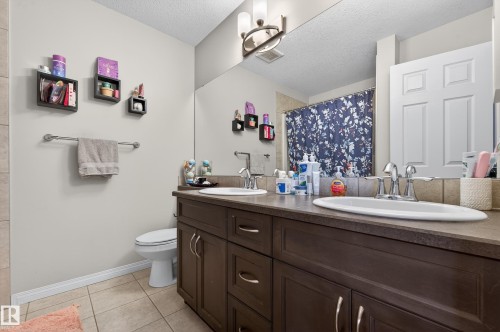 Full bath with a shower with shower curtain, double vanity, a textured ceiling, and light tile patterned floors - 5256 21 Avenue, Edmonton, AB - Indoor Photo Showing Bathroom
