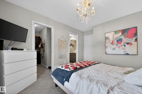 Bedroom featuring a spacious closet, carpet, a chandelier, a textured ceiling, and ensuite bath - 5256 21 Avenue, Edmonton, AB - Indoor Photo Showing Bedroom
