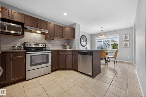 Kitchen with appliances with stainless steel finishes, dark brown cabinetry, under cabinet range hood, light tile patterned floors, and a peninsula - 5256 21 Avenue, Edmonton, AB - Indoor Photo Showing Kitchen