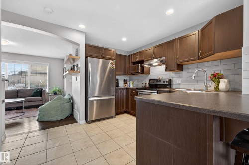 Kitchen with appliances with stainless steel finishes, dark countertops, light tile patterned floors, dark brown cabinetry, and under cabinet range hood - 5256 21 Avenue, Edmonton, AB - Indoor Photo Showing Kitchen