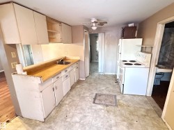 Kitchen with white appliances, a ceiling fan, open shelves, and cream cabinets - 