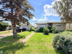 Stucco exterior residence featuring a front lawn with mature trees and established shrubbery - 