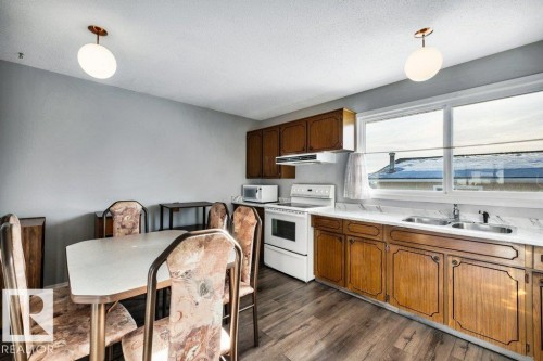 Kitchen with hanging light fixtures, white appliances, light countertops, and dark wood-type flooring - 8919 152A Avenue, Edmonton, AB - Indoor Photo Showing Kitchen With Double Sink