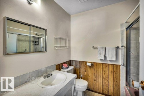 Full bath featuring vanity, shower / bath combination with glass door, a wainscoted wall, and wood walls - 8919 152A Avenue, Edmonton, AB - Indoor Photo Showing Bathroom