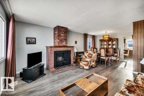 Living room featuring wood finished floors, a textured ceiling, and a brick fireplace - 8919 152A Avenue, Edmonton, AB - Indoor Photo Showing Living Room With Fireplace