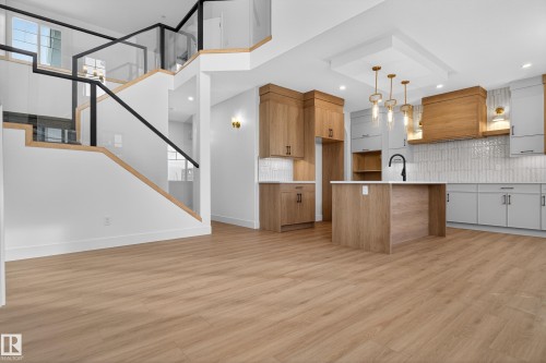 Kitchen featuring backsplash, a center island with sink, light wood-type flooring, open floor plan, and dual tone cabinetry - 26 Rosa Crescent, St. Albert, AB - Indoor Photo Showing Kitchen